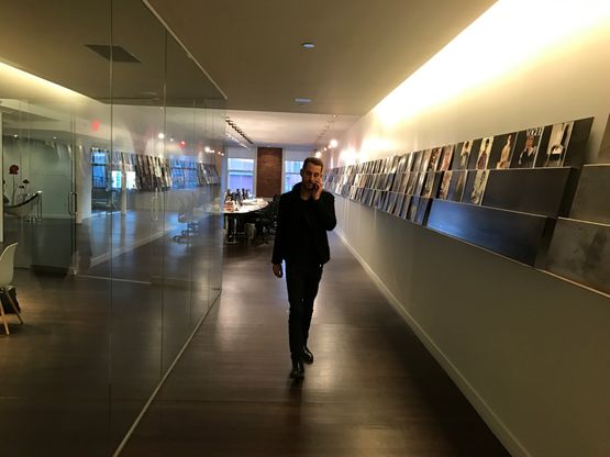 A man on the phone walking down an agency corridor lined with magazine covers.